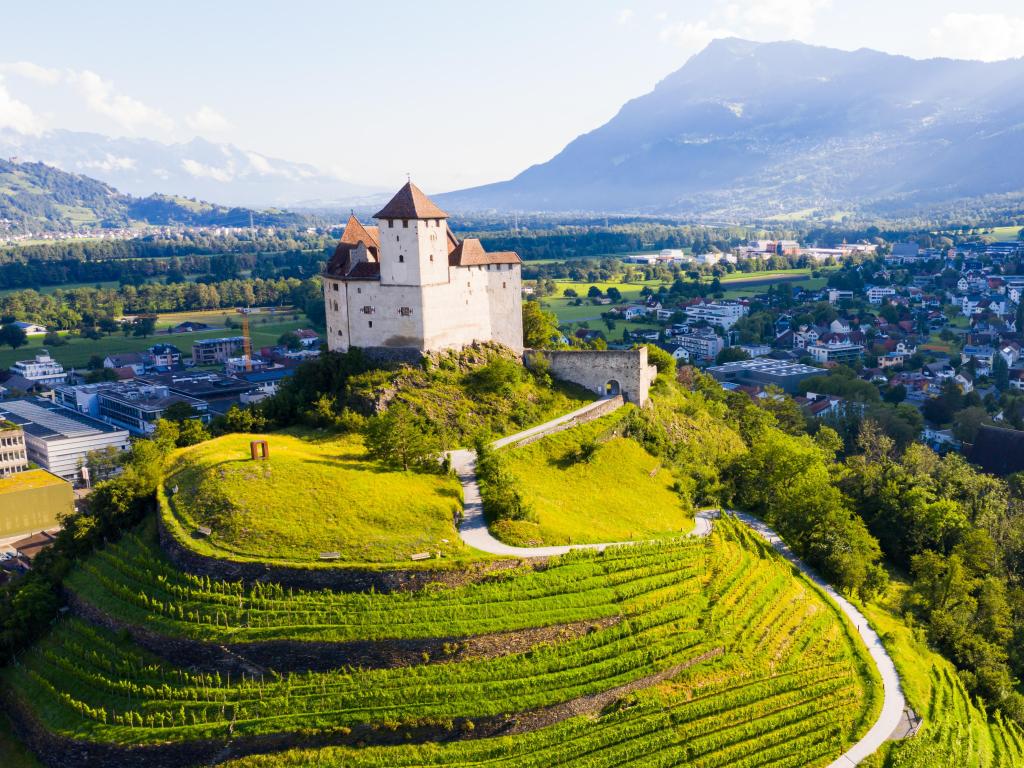 View from drone of stone Gutenberg Castle on top of green hill on background with small town of Balzers, Liechtenstein