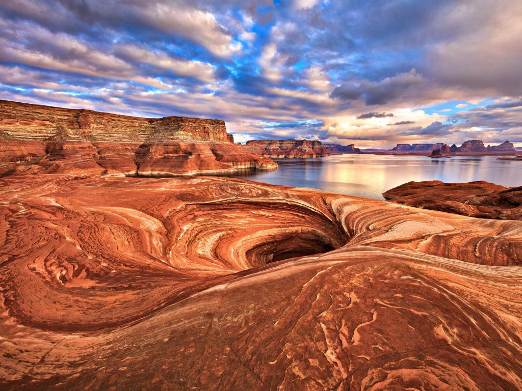 Lake Powell, Arizona, USA with stunning red rock formation along shores in the foreground, the lake and a stunning sunset in the distance. 