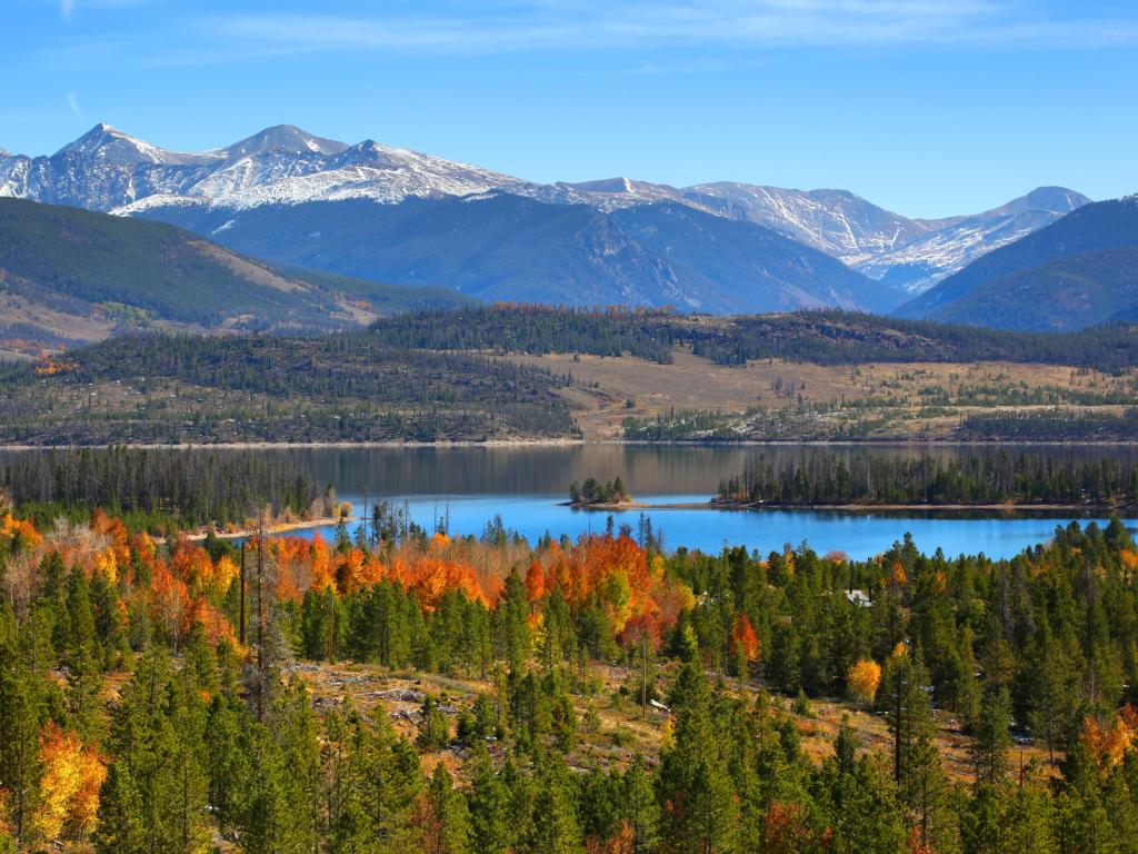 Panoramic view of Dillon Reservoir in Colorado during the fall, with orange-hued foliage in the foreground and snow-capped mountains behind the water