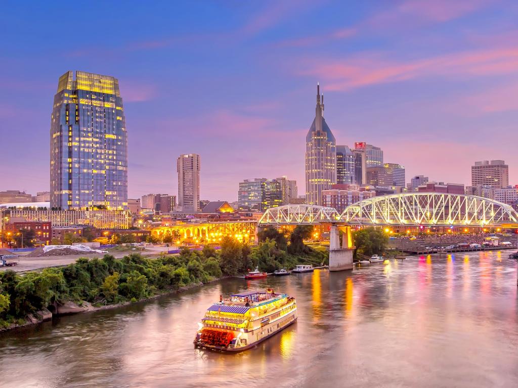 Nashville, Tennessee, USA taken at downtown skyline at twilight with a ferry in the river, the bridge and city skyline in the distance.