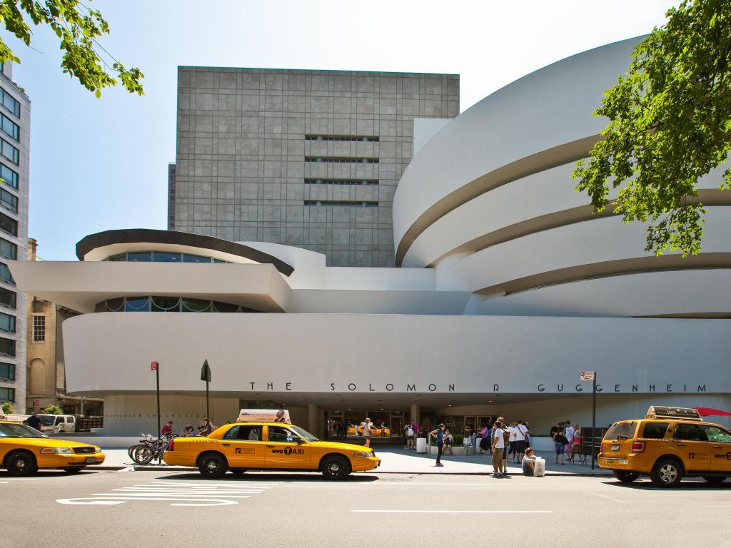 Front view of Guggenheim Museum with yellow cabs driving along the road