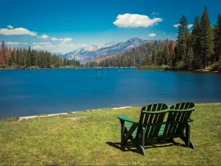 A pair of green wooden chairs on the grass overlooking peaceful Hume Lake in California on a pleasant day