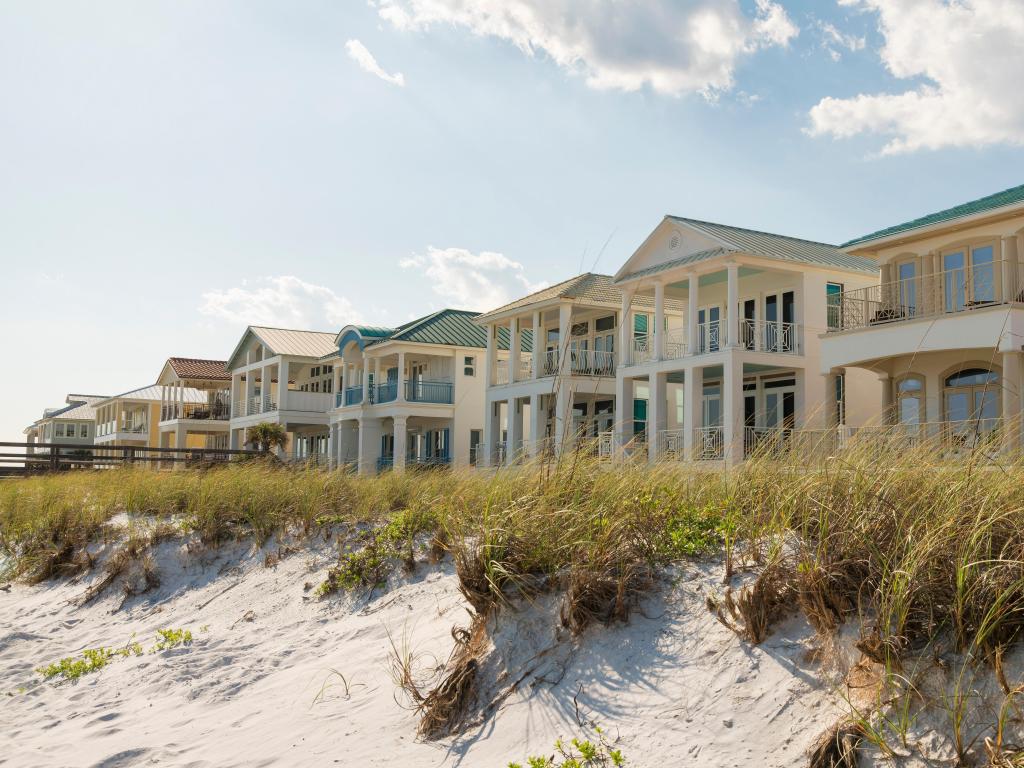 Destin, Florida, USA with white sand dunes with grasses at the front of three-storey houses at the beach. Beach houses facade with balconies against the sky.