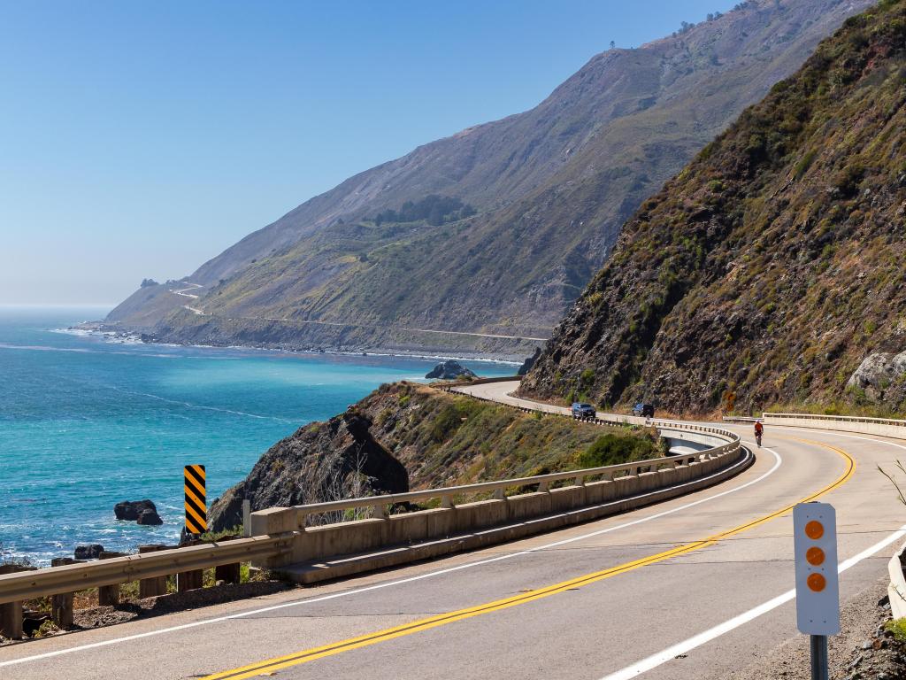 The Pacific Coast Highway road winding around the mountains and ocean on a sunny day