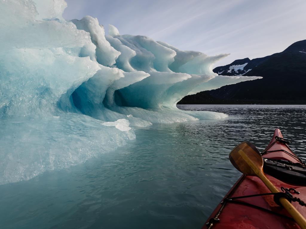 Paddler pauses journey to enjoy the splendor of the shapes of the melting Iceberg in summertime Alaska's Kenai Fiords National Park