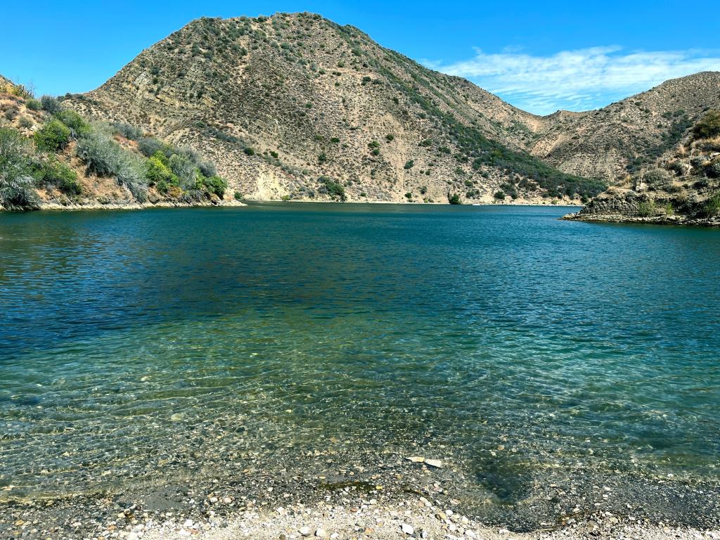 San Bernadino National Forest, California, USA with a private beach view of beautiful Pyramid Lake with stones in the foreground and the blue turquoise water with green mountain and blue skies.