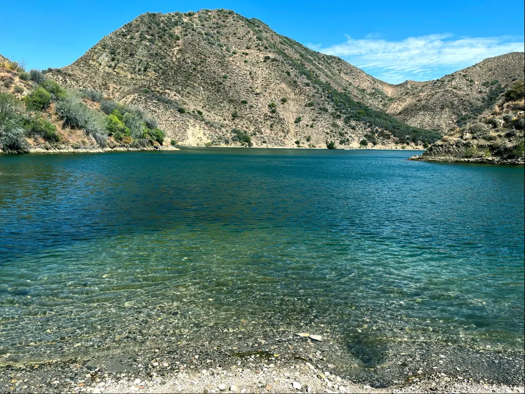 San Bernadino National Forest, California, USA with a private beach view of beautiful Pyramid Lake with stones in the foreground and the blue turquoise water with green mountain and blue skies.