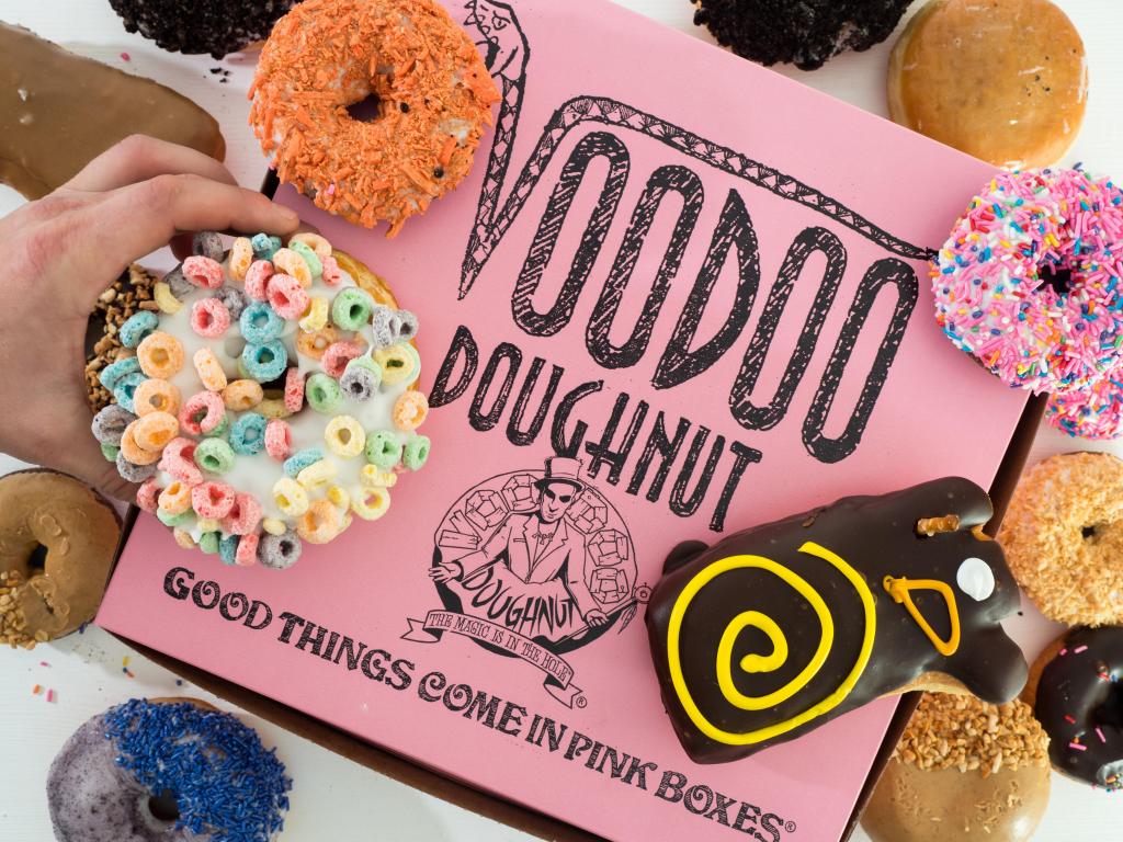 A pink donut box with several colorful donuts placed on it, hand picking one up