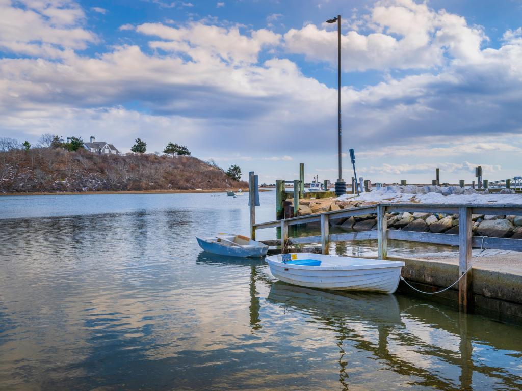 Cumulous clouds and water reflections at Harwich harbor with empty boats and dinghy mooring tied to the commercial dock.