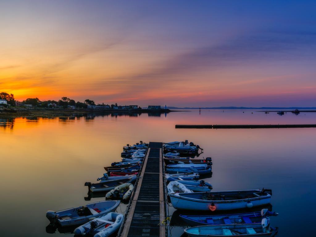 Sunrise over calm ocean with small boats moored off a narrow jetty