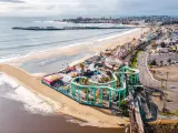 Aerial drone shot of Santa Cruz Beach Boardwalk, with the colourful amusement park next to the beach with mountains in the background.