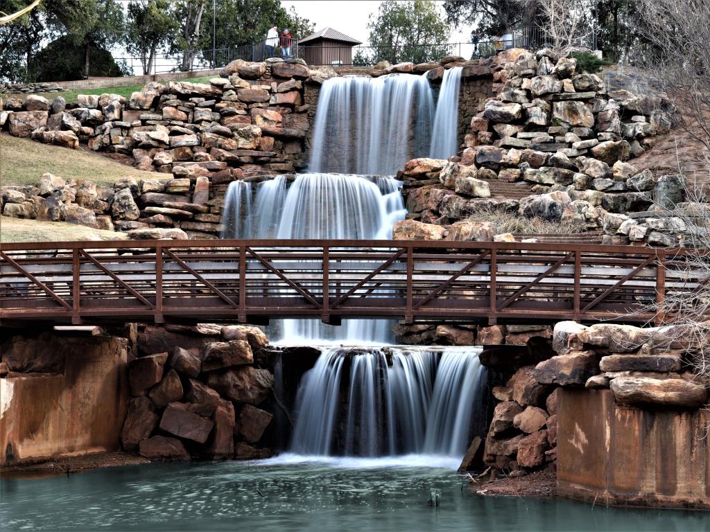 Four tier water fall surrounded by rocks with walking bridge in Wichita Falls Texas.