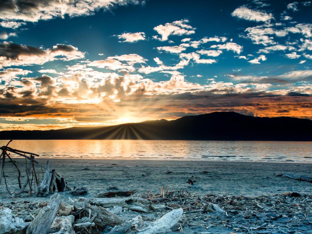 Dramatic cloudscape and Sunset flare over silhouetted Kapiti island at Paraparaumu beach covered in driftwood and beach art