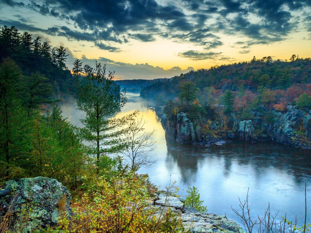 St Croix Falls, Wisconsin, USA with a view of the river at sunset with trees and rocks surrounding.
