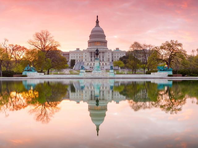 Washington DC, USA with a panorama view of The United States Capitol building taken at sunrise and reflecting in the lake in the foreground.