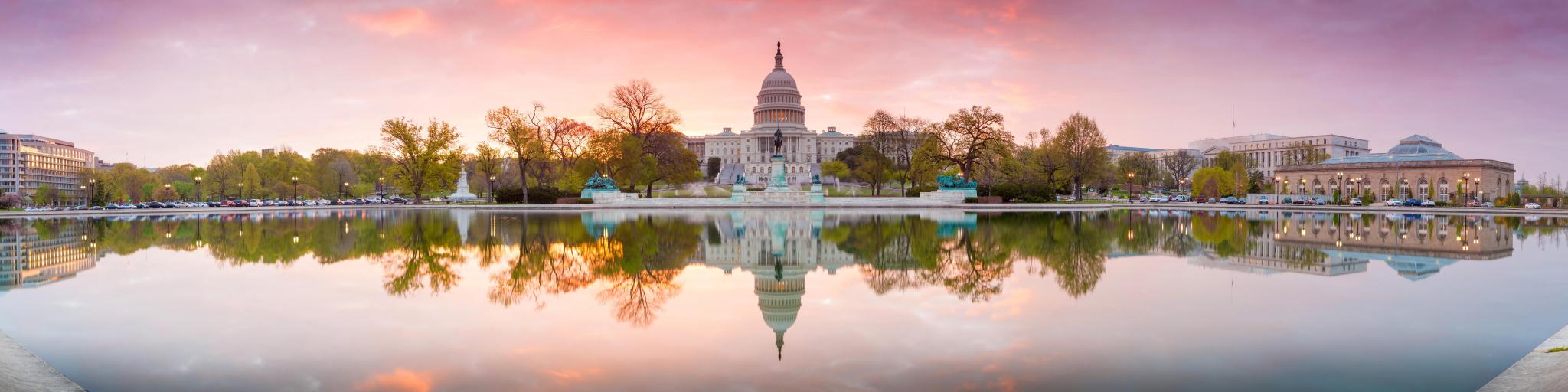 Washington DC, USA with a panorama view of The United States Capitol building taken at sunrise and reflecting in the lake in the foreground.