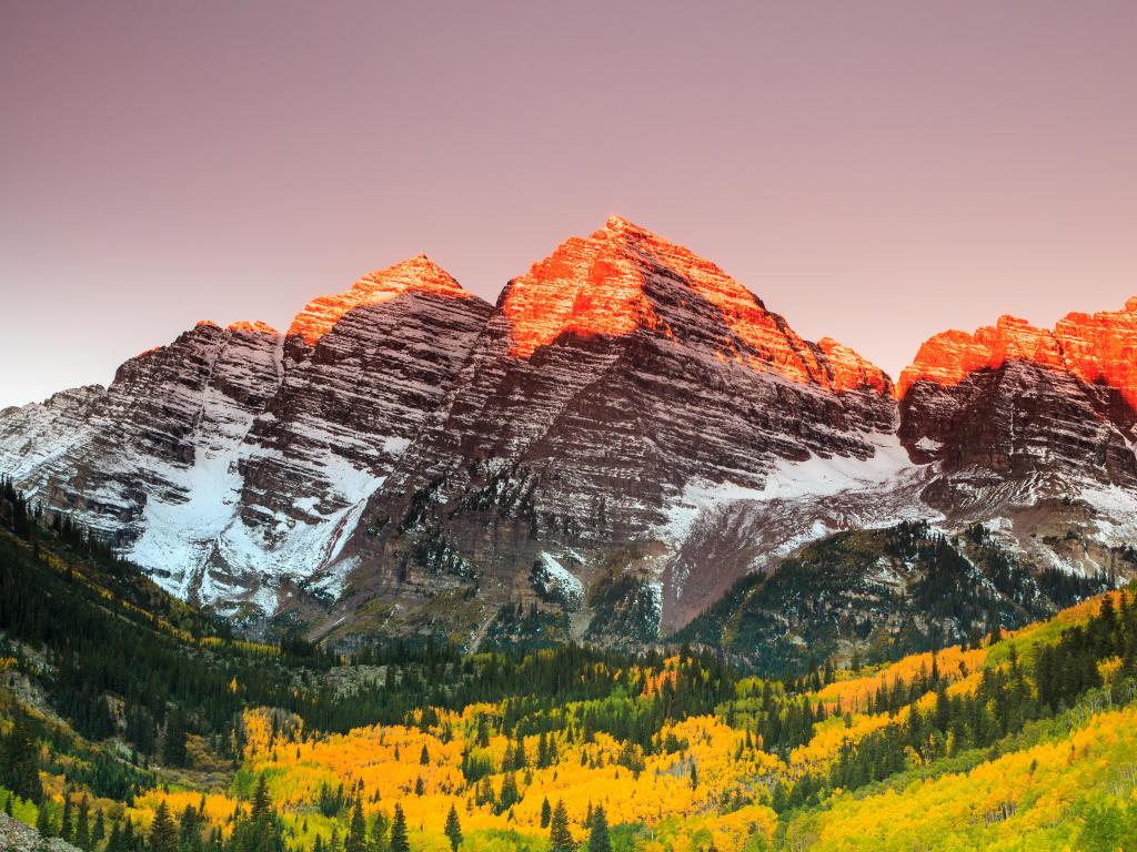 White River National Forest, Colorado, USA taken at Maroon Bells during sunrise with the stunning snow-capped mountains in the distance and trees in the foreground.