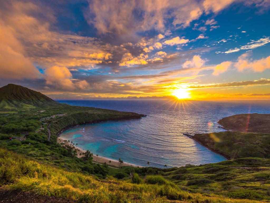 Panoramic shot of Hanauma Bay on Oahu, Hawaii at sunrise, with an amber glow cast onto the wispy clouds above