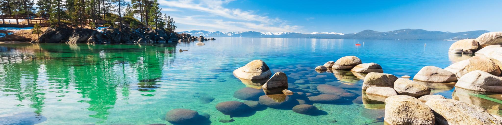 Lake Tahoe, USA with a rocky shoreline in sunny day, beach with blue sky over clear transparent water.
