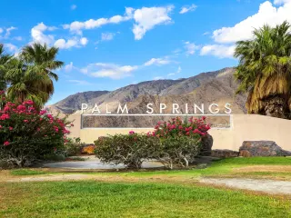 Welcome Sign surrounded by bushes and palms with the mountains in the background