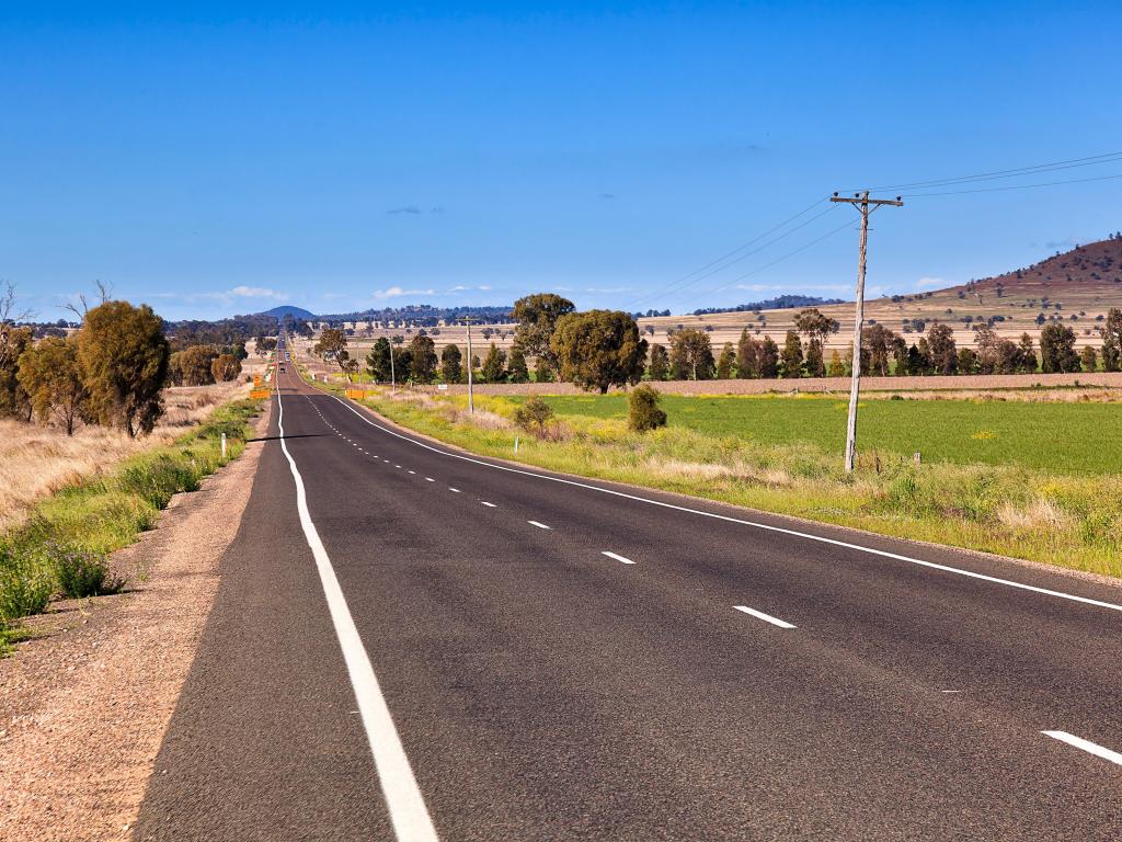 Long, straight road across wide, flat grassy fields with small hill to one side