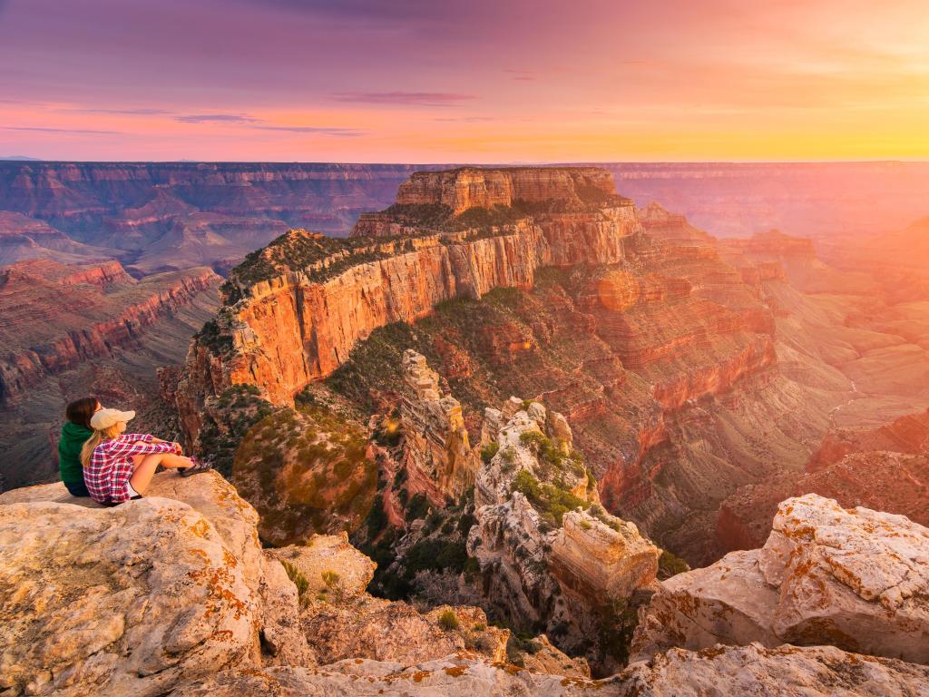 A group of people was sitting near the edge watching sunset at Grand Canyon National Park North Rim, USA. 