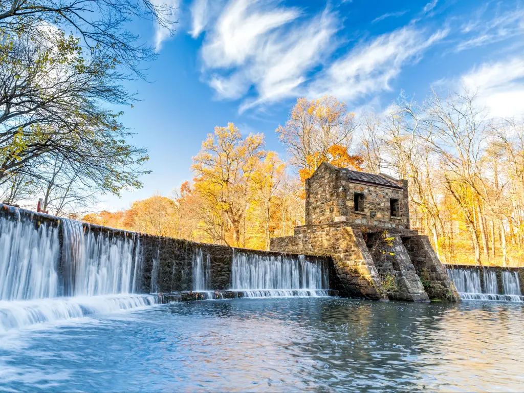 Wide view of Speedwell Dam, with rushing water cascading down dam walls against blue skies and calm lake, New Jersey