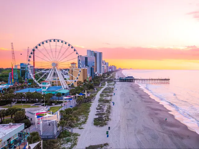 Myrtle Beach with its famous pier and Ferris Wheel in the background during a pink and peach sunset.