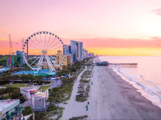 Myrtle Beach with its famous pier and Ferris Wheel in the background during a pink and peach sunset.
