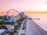 Myrtle Beach with its famous pier and Ferris Wheel in the background during a pink and peach sunset.