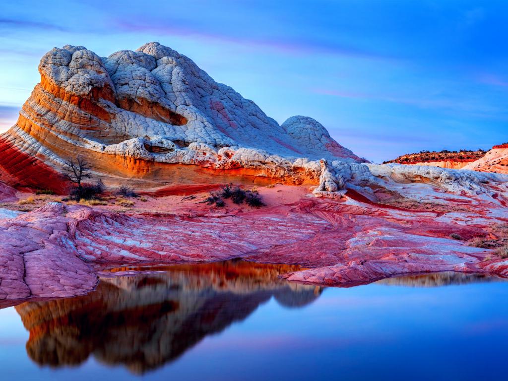 A beautiful bluff of sandstone the white pockets and wave-like red and white canyon rock formation in Vermillion Cliffs reflecting the water during sunset