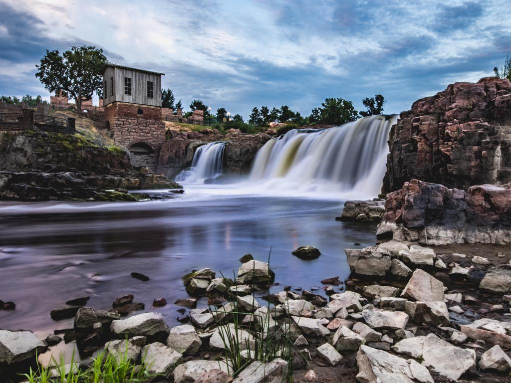 Falls Park, Sioux Falls, South Dakota, USA with rocks and a waterfall in the foreground and a building on the upper part of the rocks taken just before sunset. 