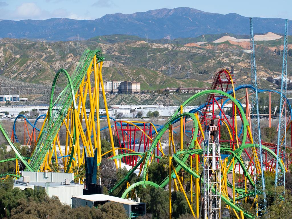 Wide view of colorful roller coaster rides at an amusement park, sunny day mountains in background. Six Flags Magic Mountain