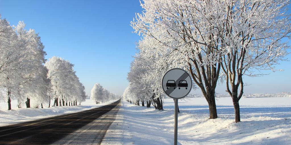 An overtaking prohibited roadsign on the side of an empty main road, with blue sky and snow on the ground and in the trees