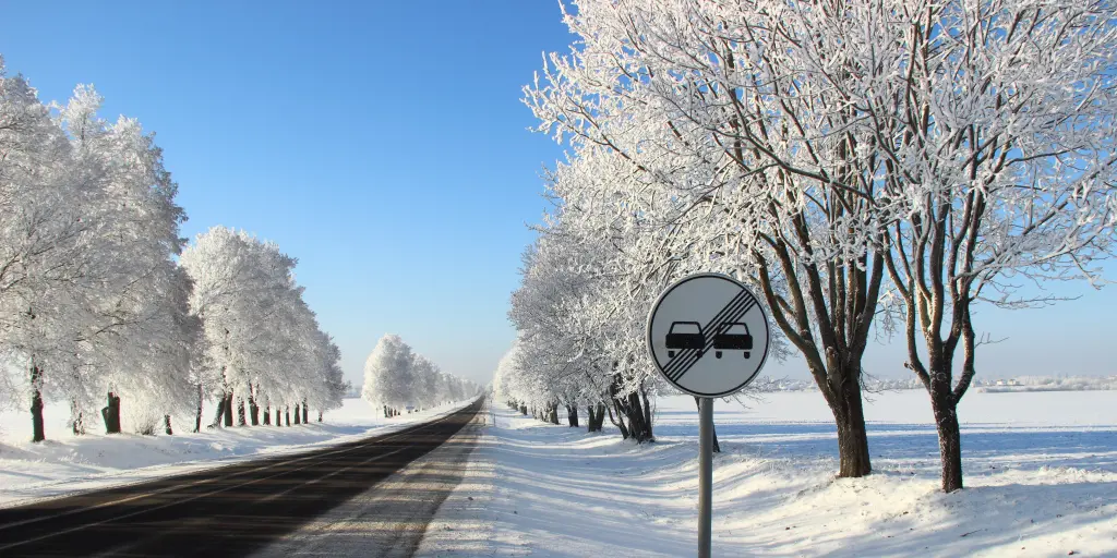 An overtaking prohibited roadsign on the side of an empty main road, with blue sky and snow on the ground and in the trees