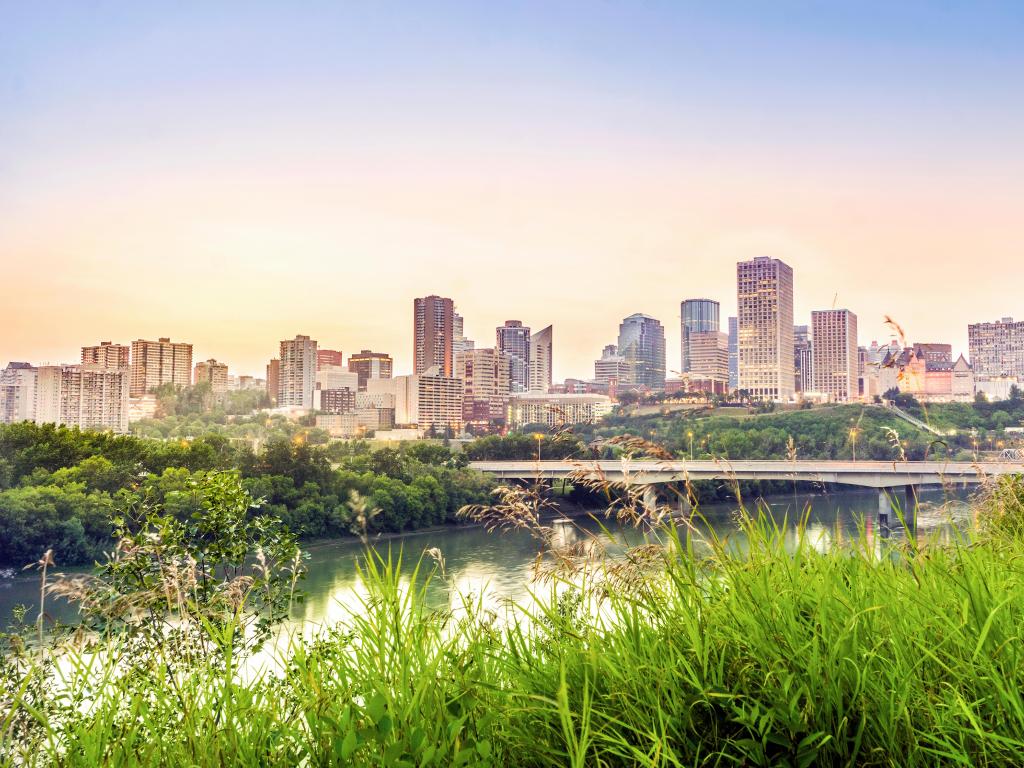 Edmonton, Alberta, Canada with the downtown city in the distance taken after sunset, lush grasses in the foreground and the river between the two.