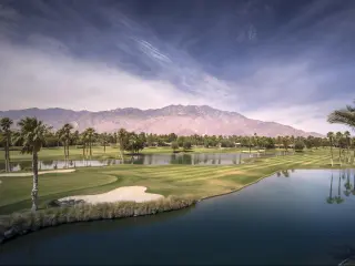 Palm Springs, California, USA with a beautiful landscape view of Palm Springs and Chino Canyon on a hot summer day, with a lake in the foreground and palm trees between the two.