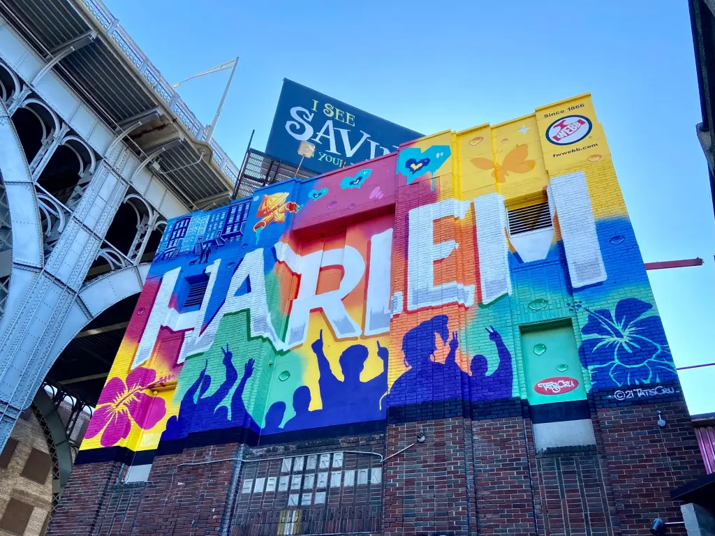 Colorful mural on the side of a building, reading "Harlem" on a sunny day
