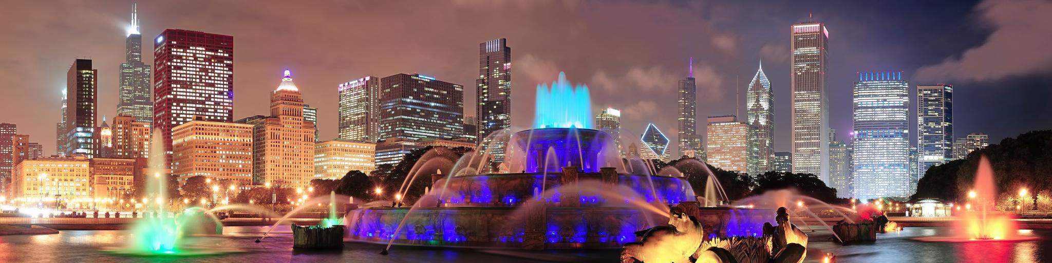 A panoramic view of night-lit and skyscrapers of Chicago with Buckingham fountain in Grant Park at the front