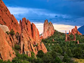 Red rock formations rising above trees during a dramatic sunset