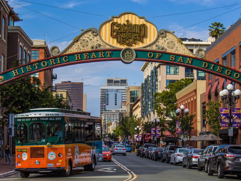 Orange trolley bus drives under sign saying 'historic heart of San Diego' in the sunshine