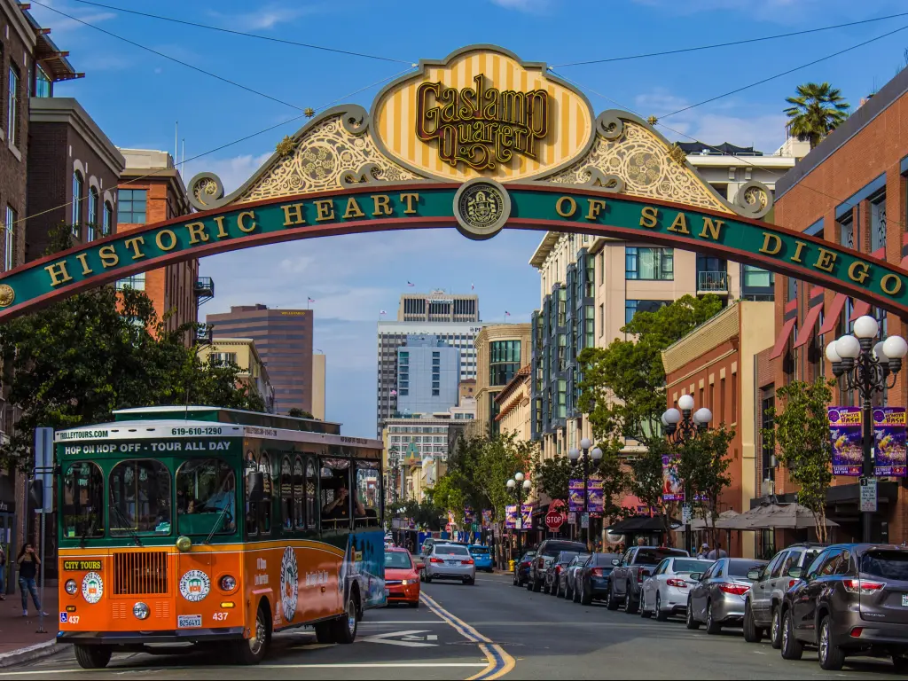 Orange trolley bus drives under sign saying 'historic heart of San Diego' in the sunshine