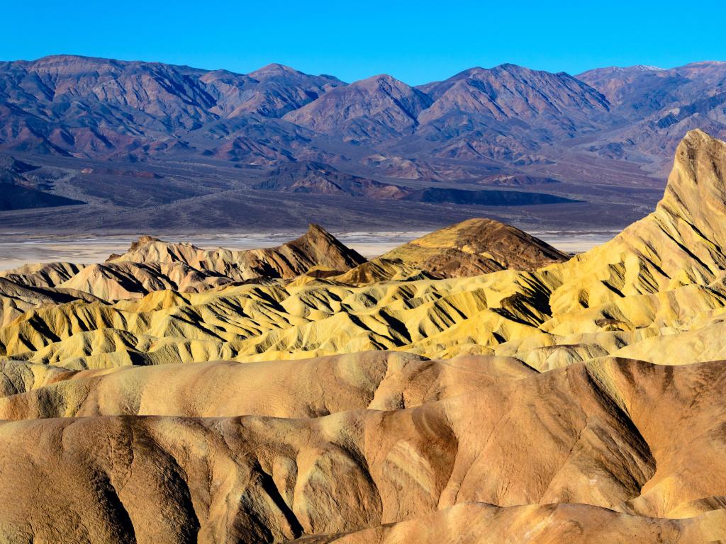Death Valley National Park with golden rock formations at the foreground and darker mountains in the background. 