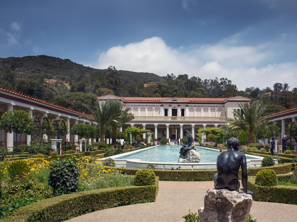 Pool, roman style villa with columns, mountains behind, statue