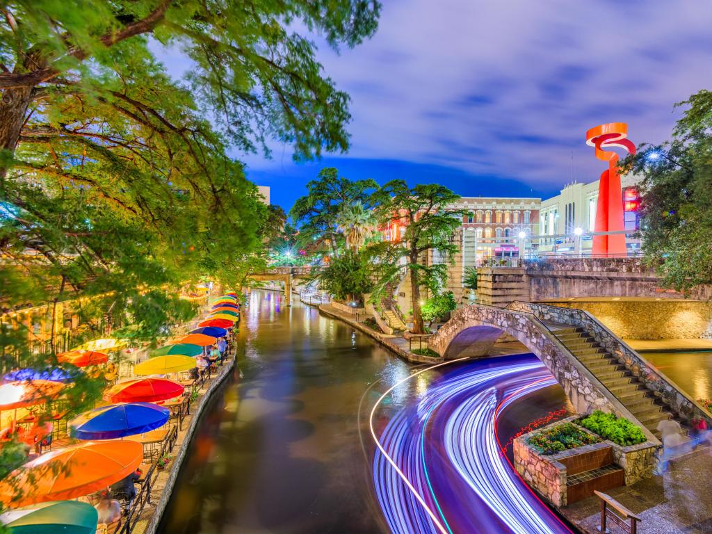 San Antonio, Texas, USA with the cityscape on the River Walk taken at night with colorful umbrellas and trees overhanging the river.