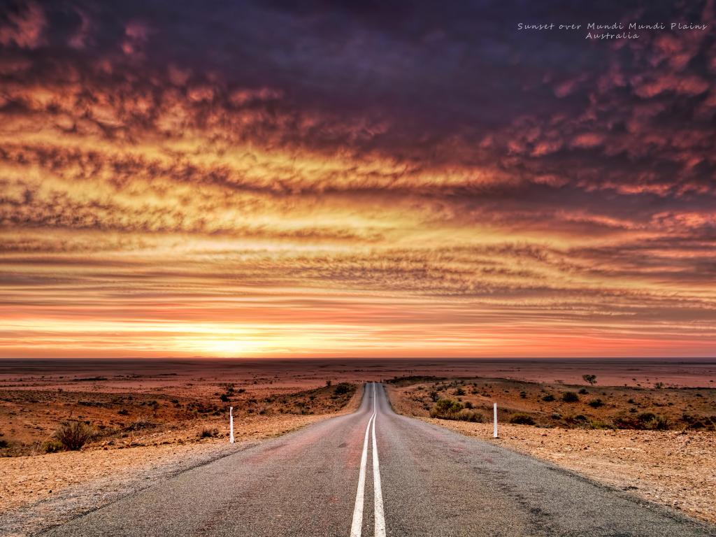 A fiery sunset over the plains, with a highway in the middle of the image, disappearing into the horizon