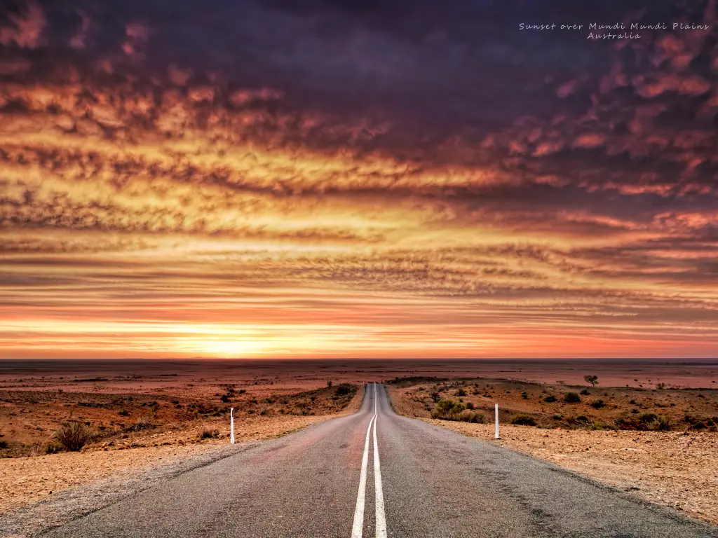 A fiery sunset over the plains, with a highway in the middle of the image, disappearing into the horizon