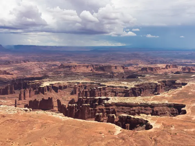 View of red canyons below from a high point in Canyonlands National Park, with cloudy sky visible in the horizon