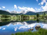 Sprague Lake surrounded by trees with mountains in the background, with their reflection on a mirror-like lake