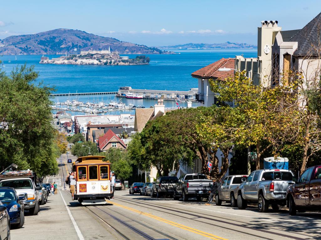 San Francisco street with a historic cable car driving uphill. Sunny day with the sea in the background